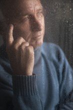 Lonely man sitting behind a window covered in rain drops