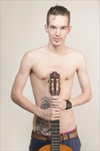 Bare-chested young man with tattoo holding a guitar