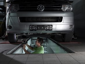 Mechanic standing in a pit checking the brake discs of a VW transporter