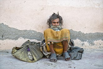 Beggar leaning against a house wall