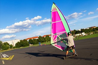 Windskater practicing on the asphalt runway with a windsurfer sail and a longboard