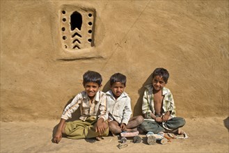 Three boys sitting outside a mud house