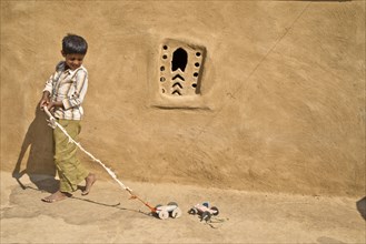 Boy playing with a home-made toy cars outside a mud house