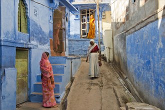 Four women in traditional saris in an alleyway with blue houses