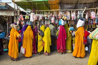 Indian women in colorful saris standing in front of a stall selling toys and fashion jewellery