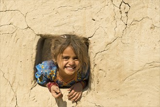 Little girl leans out of a window opening in a mud house