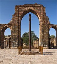 Entrance portal of the Quwwat-ul-Islam Masjid Mosque with relief decorations and an iron pillar in the courtyard