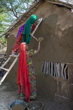 Two women wearing traditional saris rendering a house wall with a mixture of clay