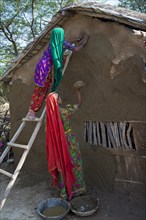 Two women wearing traditional saris rendering a house wall with a mixture of clay