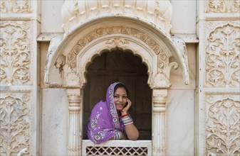 Young friendly Indian woman wearing a headscarf looking out of a window opening of an ornate marble facade