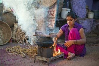 Young Indian woman squating on the ground and preparing a meal on a hotplate