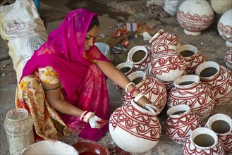 Indian woman wearing a headscarf sitting on the floor and painted clay water jars with traditional ornamentations