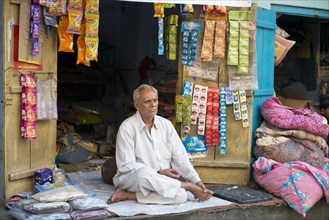 Senior Indian man sitting on a blanket in front of his stall