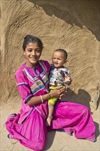 Friendly smiling girl in traditional dress holding a small boy in her arms