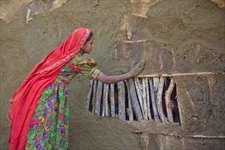 Girl in traditional dress plastering the wall of a house with a mixture of water