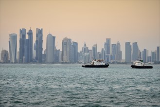 Tugboats in front of the skyline of Doha at dusk