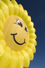 Hot air balloon in the shape of a "laughing" sun or sunflower against a blue sky