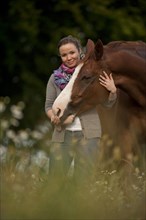 Woman standing next to a Hanoverian horse in a meadow