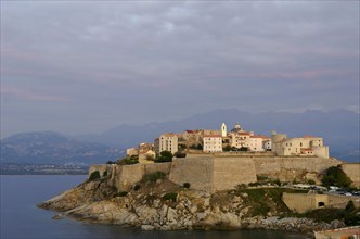The citadel (castle) of Calvi surrounded by the mediterranean sea in front of the steep mountains of Corsica. Calvi is in the department Haute-Corse