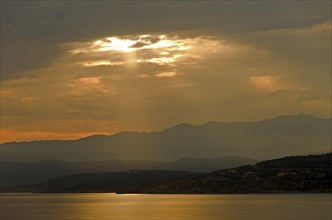 The rising sun forms sun beams behind the rocks of the island Ile de la Pietra near L'Île-Rousse. L'Île-Rousse  is in the department Haute-Corse