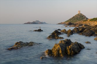 The genoese tower Tour de la Parata at the right and the islands Les Iles Sanguinaires behind the rocky mediterranean coast illuminated by warm morning light. Les Iles Sanguinaires are in the departme...