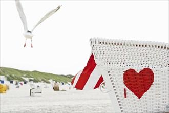 Roofed wicker beach chair with a red heart on the beach and a seagull in flight