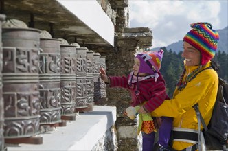 Young mother wearing yellow cloths and her little child turning prayerwheels