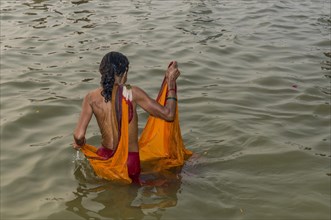 Woman wearing an orange sari taking a bath in the Sangam