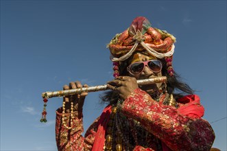 Colourfully costumed devotee playing flute during Kumbh Mela