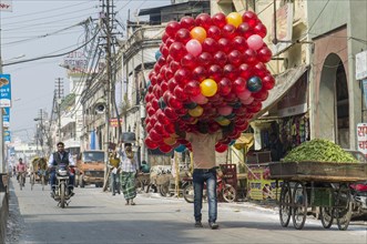 Man carrying a huge pack of red toy balls along a street