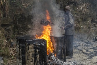 A worker heating tar in barrels with an open fire at a road construction site
