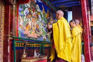 Three monks of Lamayuru Gompa are praying in front of a colorful religious wall painting