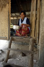 Woman holding a pot at the entrance of her traditional stilt house made of wood and bamboo