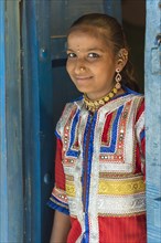 Young girl in traditional colorful clothes standing in a door