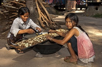 Khmer woman and a girl filling caramelized palm sugar into small moulds made of strips of palm leaves for the production of traditional palm sugar candies