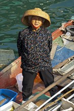 Old Chinese fishmonger with straw hat on her boat