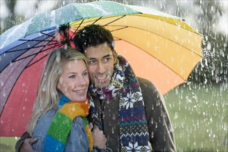 Smiling couple with a colourful rainbow umbrella is enjoying the rain