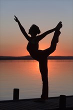 Silhouette of a woman practicing yoga against the light of the evening sun