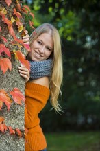 Young woman looking from behind a wall with colorful autumn leaves