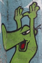 Green cartoon character holding up its hands