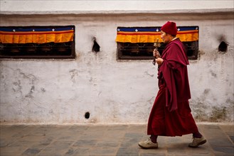 Buddhist monk walking around Boudhanath stupa with a prayer wheel