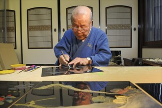 Japanese artisan scraping a bamboo motif onto the top lacquer coat