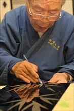 Japanese artisan scraping the top lacquer coat away to carve out golden bamboo leaves