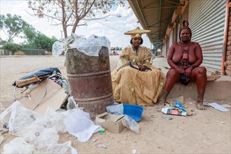 Herero woman and Himba woman woman in traditional dress sitting next to rubbish