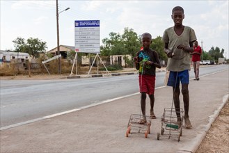 Two Himba boys playing with their self-made toy cars by the roadside