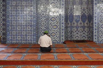 Man in prayer in front of a wall with Iznik faience tiles