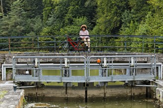 Spectator with a bicycle observing a houseboat passing through a lock on the Canal des Vosges