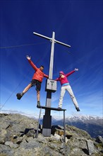 Hikers on the summit cross on the summit of Boeses Weibele Mountain in the Defregger Group