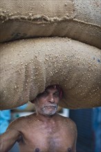 Elderly man carrying two bags filled with spices on his head