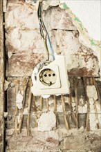 A damaged power socket hanging from a wall in a dilapidated house